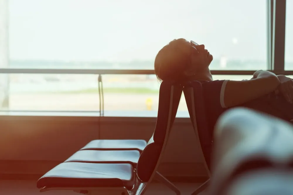 Woman backlit by airport window resting her head on a chair in an airport terminal